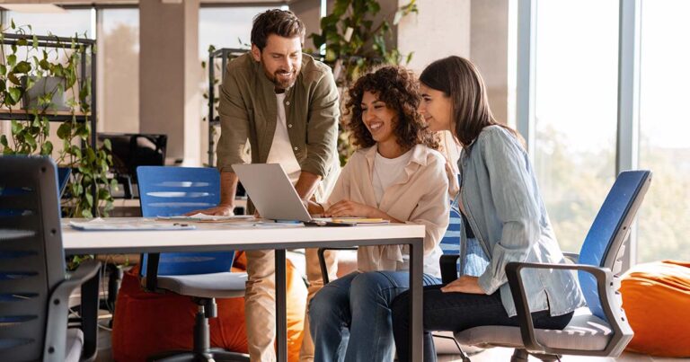 Three marketing managers are collaborating on a project, using a laptop in a modern office space with natural light and comfortable seating