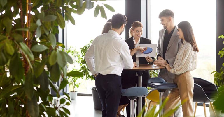 Business team gathered in office surrounded by greenery, discussing charts and financial results.