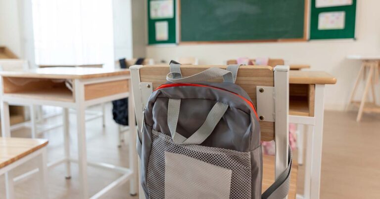 Background of study table and chairs with backpacks in empty classroom.