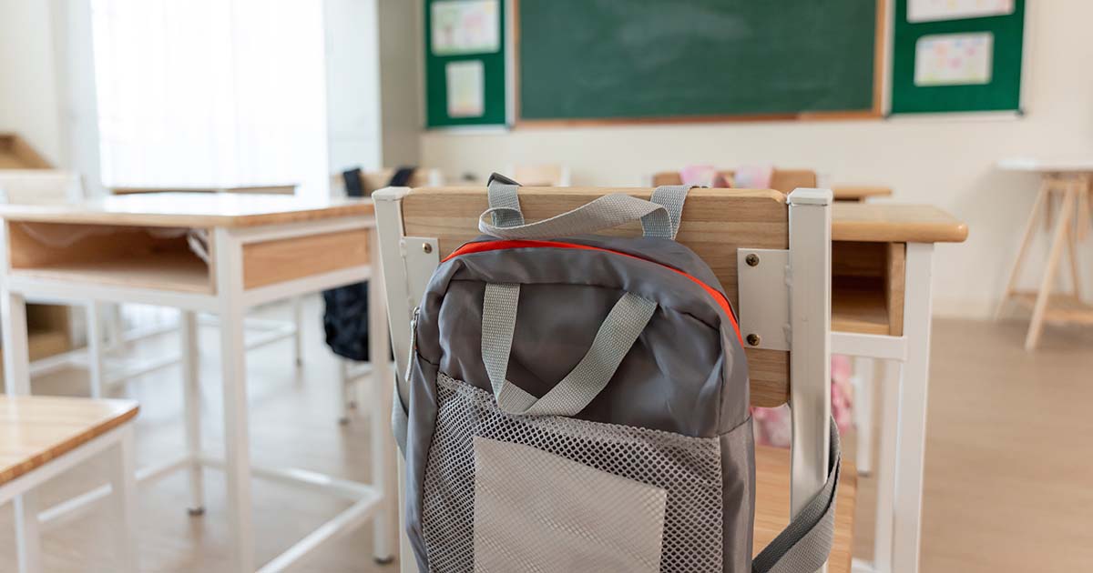 Background of study table and chairs with backpacks in empty classroom.
