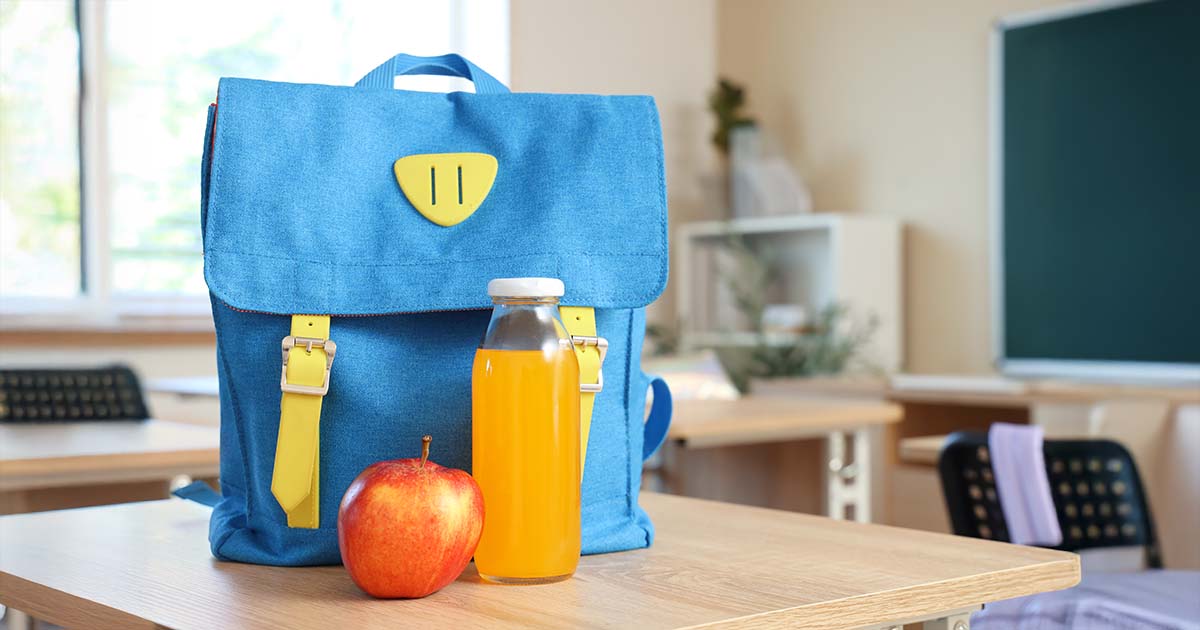 Blue backpack with apple and juice on desk in classroom
